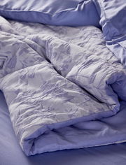 Nahaufnahme einer lila Bettwäsche mit floralem Muster, auf einem Bett drapiert.