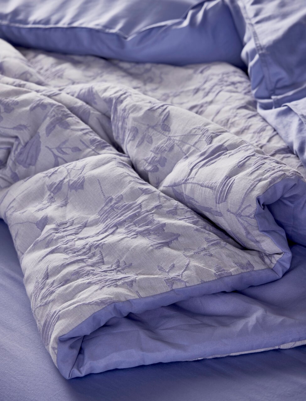 Nahaufnahme einer lila Bettwäsche mit floralem Muster, auf einem Bett drapiert.