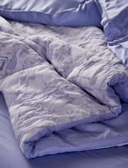 Nahaufnahme einer lila Bettwäsche mit floralem Muster, auf einem Bett drapiert.