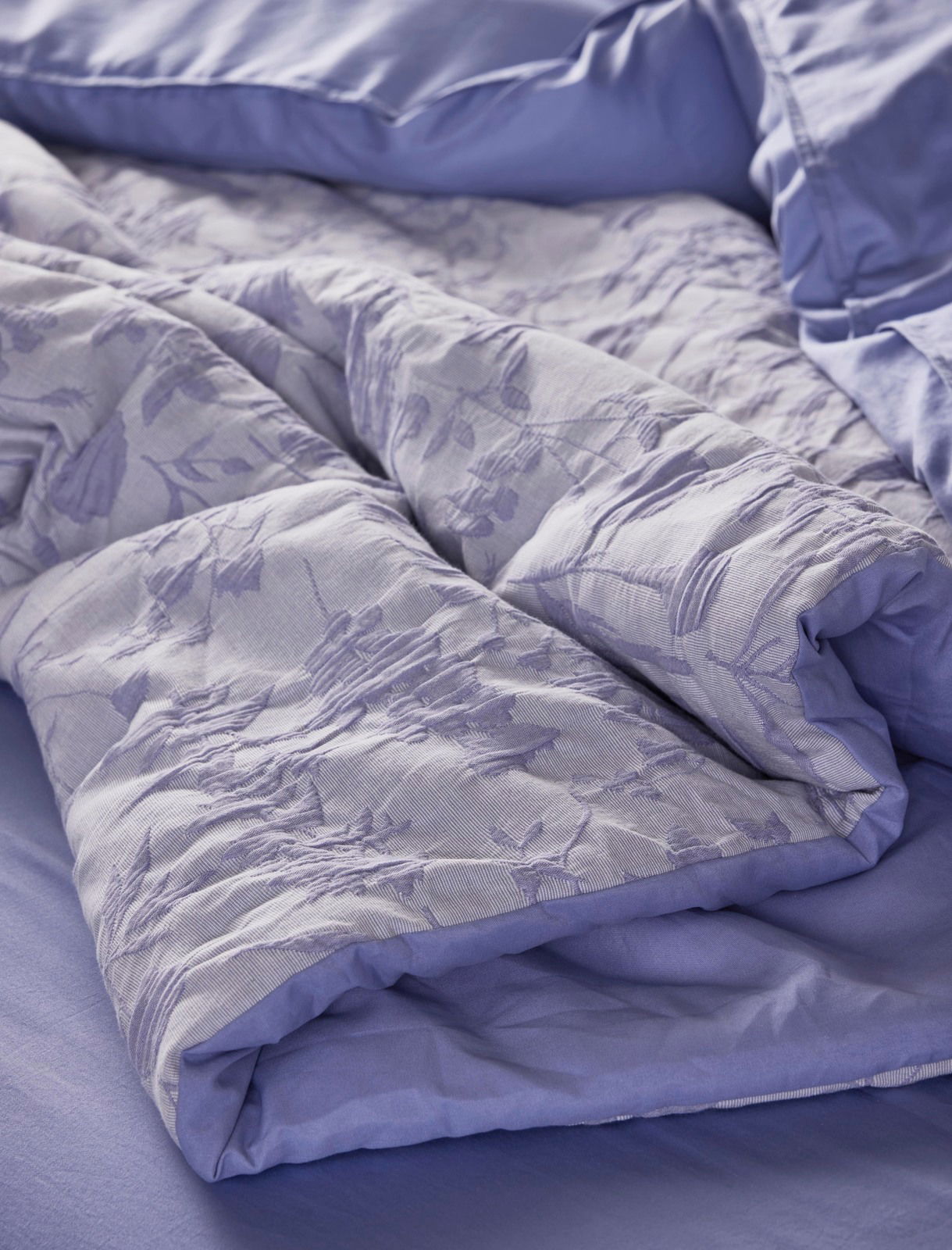 Nahaufnahme einer lila Bettwäsche mit floralem Muster, auf einem Bett drapiert.