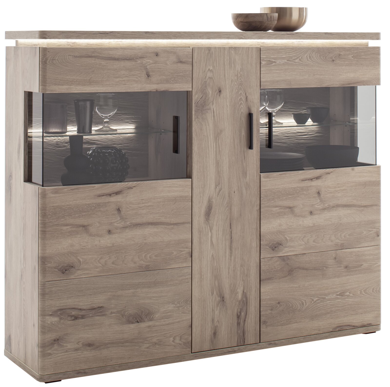 Moderne Highboard-Vitrine aus hellem Holzdekor mit zwei Glasvitrinenfächern, LED-Beleuchtung und schwarzen Griffen, frontal in leichter Schrägansicht von vorn links auf weißem Hintergrund