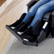 Nahaufnahme eines Massagesessels mit Fokus auf die Bein- und Fußstütze, in der eine Person mit Jeans sitzt.