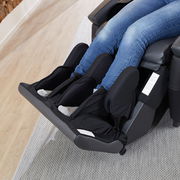 Nahaufnahme eines Massagesessels mit Fokus auf die Bein- und Fußstütze, in der eine Person mit Jeans sitzt.