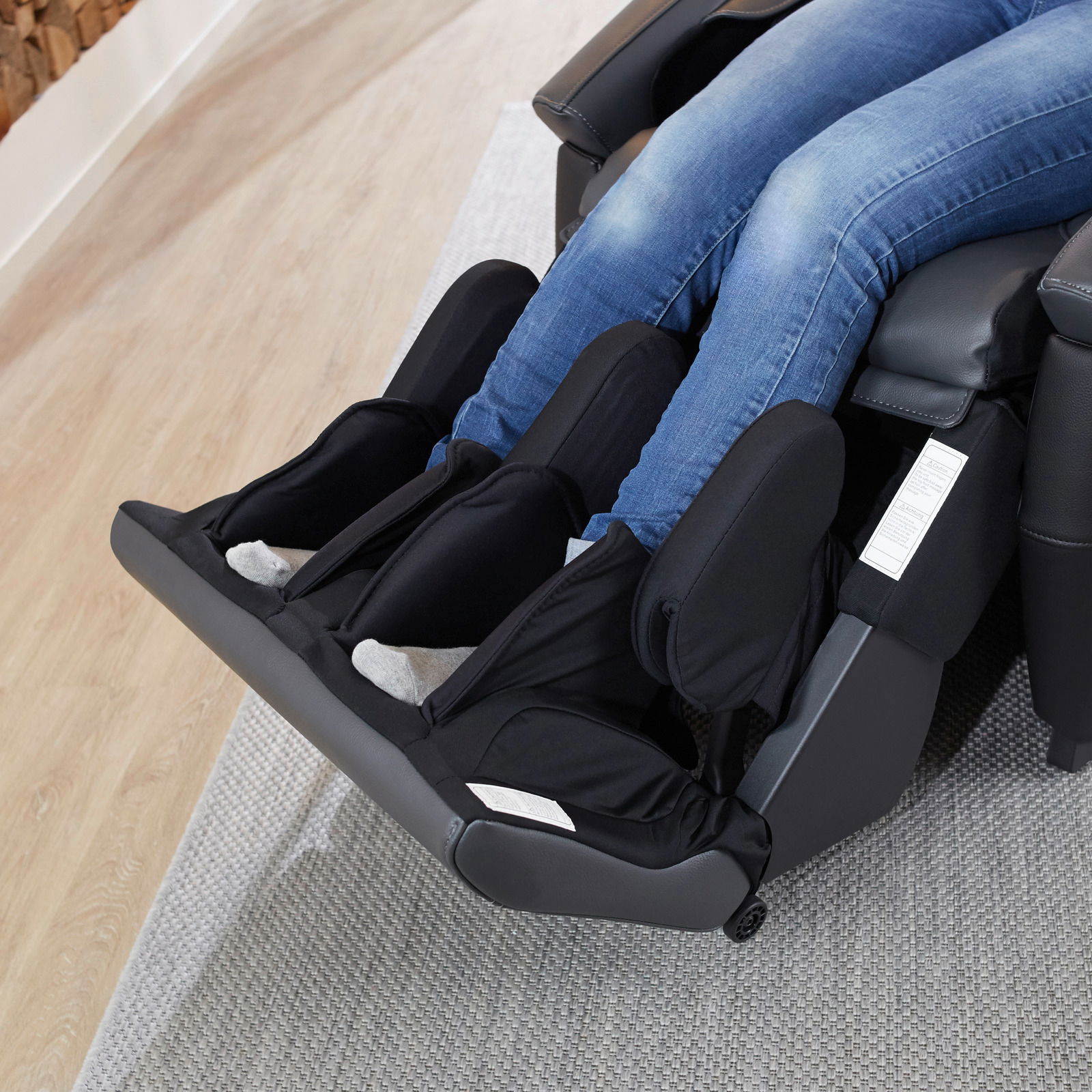 Nahaufnahme eines Massagesessels mit Fokus auf die Bein- und Fußstütze, in der eine Person mit Jeans sitzt.