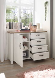 Weiße Kommode mit offenen Schubladen und Tür, dekoriert mit Büchern und Vasen, in einem hellen Raum mit Blick aus dem Fenster.