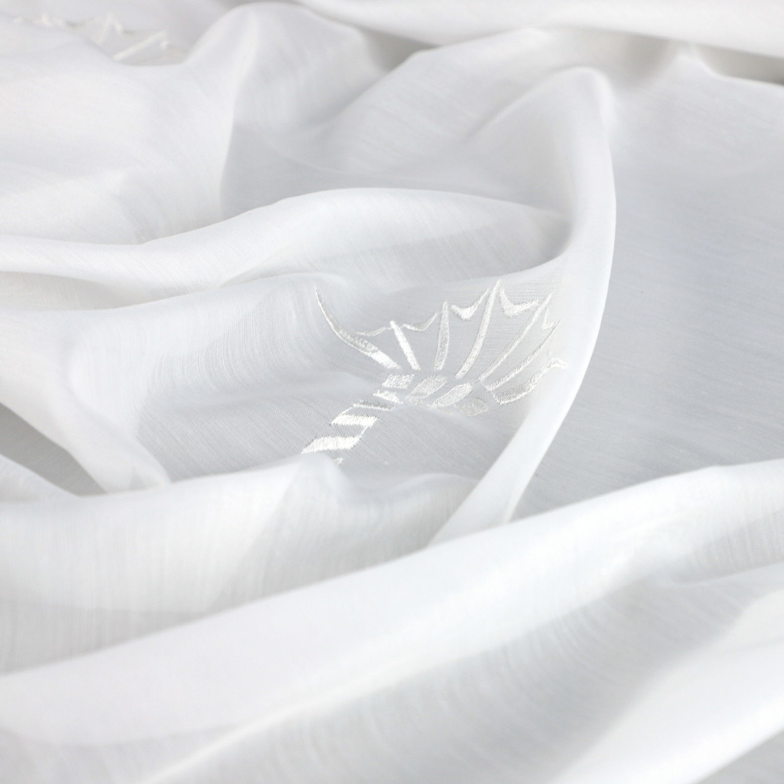 Nahaufnahme eines weißen Vorhangs mit dezentem Blattmuster, ausgebreitet in weicher, fließender Perspektive.