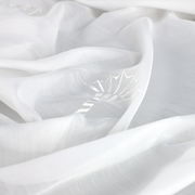 Nahaufnahme eines weißen Vorhangs mit dezentem Blattmuster, ausgebreitet in weicher, fließender Perspektive.