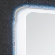 Nahaufnahme eines beleuchteten Spiegels mit abgerundeten Ecken, montiert an einer Wand mit dunklem Muster.