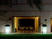 Zwei beleuchtete Blumentöpfe Melisa 50 vor einem großen Fenster, nachts im Garten platziert, mit Blick auf das Haus.
