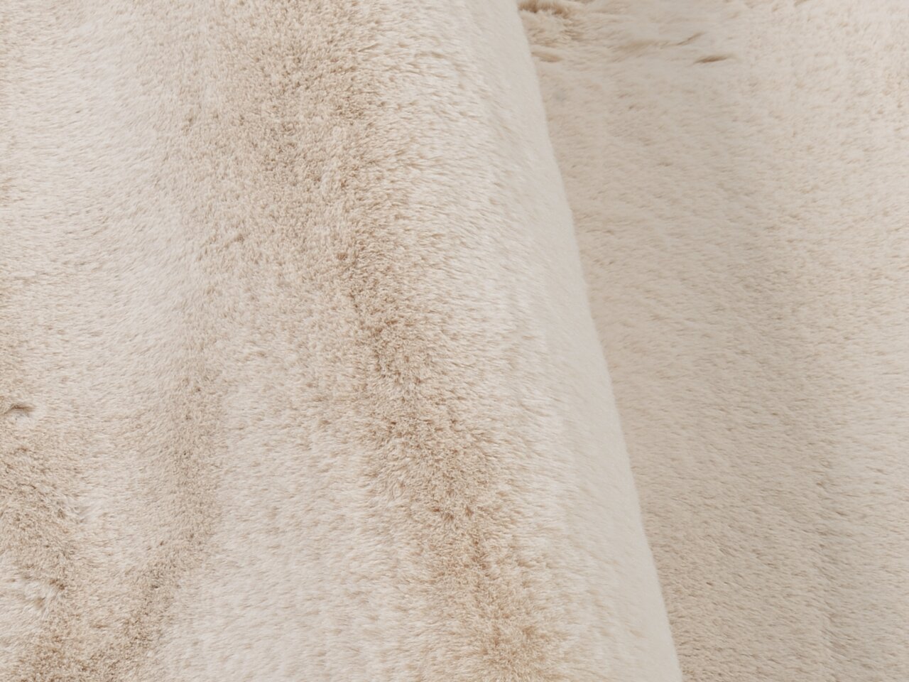 Nahaufnahme eines weichen, beigen Fellteppichs mit flauschiger Textur.
