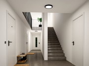 Moderner, heller Flur mit runder schwarzer Deckenleuchte, grauer Treppe rechts und weißen Türen, perspektivisch aus der Frontansicht mit Blick in den Gang nach hinten