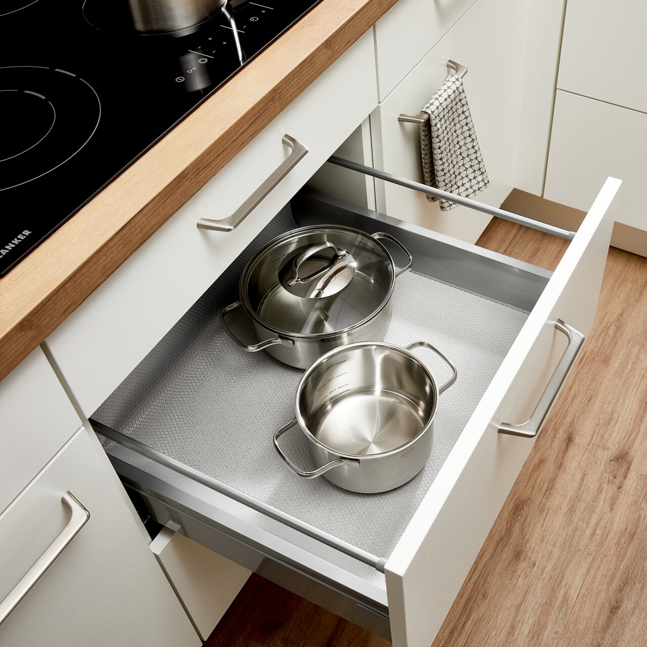 Offene Küchenschublade mit Schubladenmatte und zwei Edelstahltöpfen, von oben fotografiert.