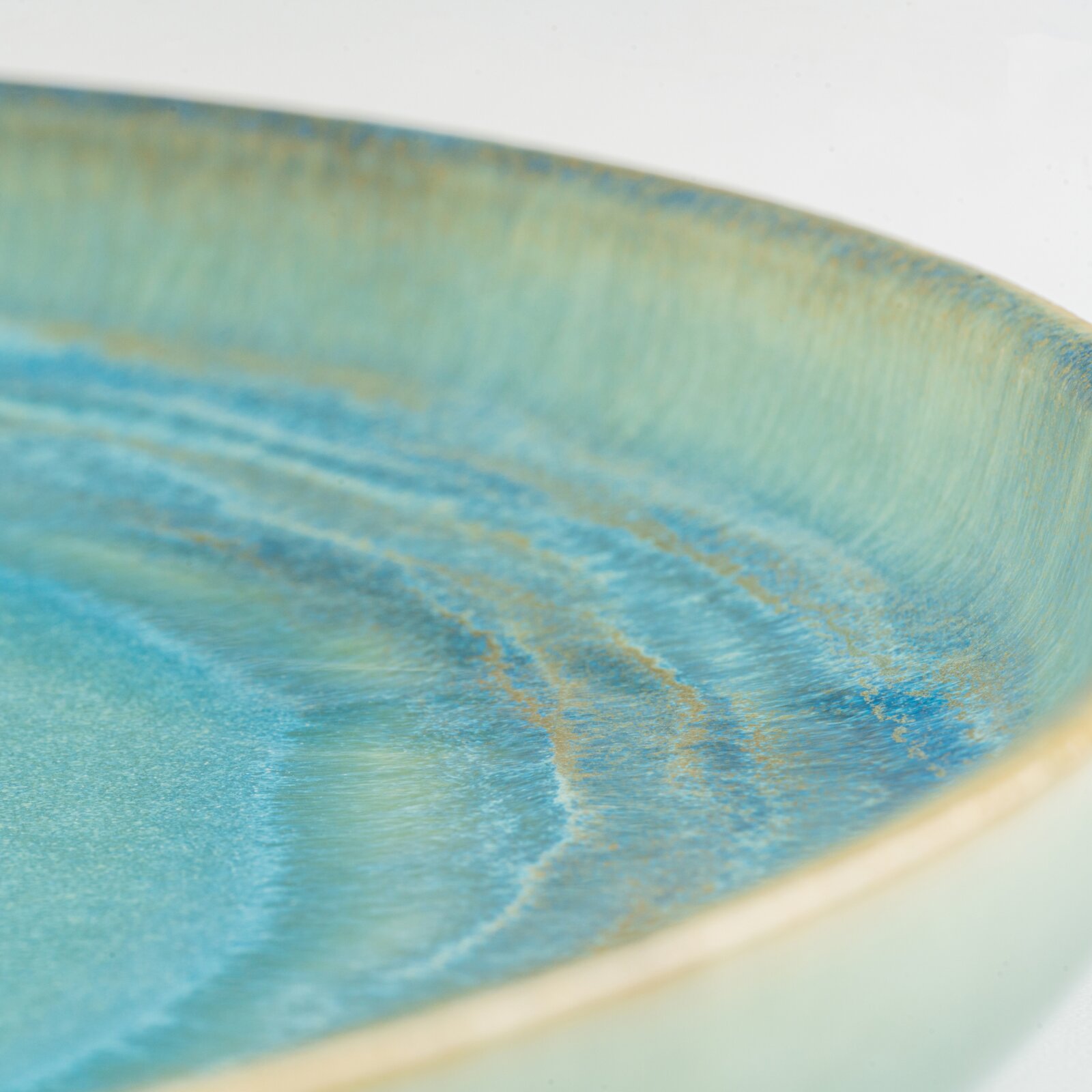 Detailaufnahme aus schräger Seitenperspektive: blau-türkis glasierte Keramikschale mit feiner, goldbrauner Sprenkelstruktur am Rand