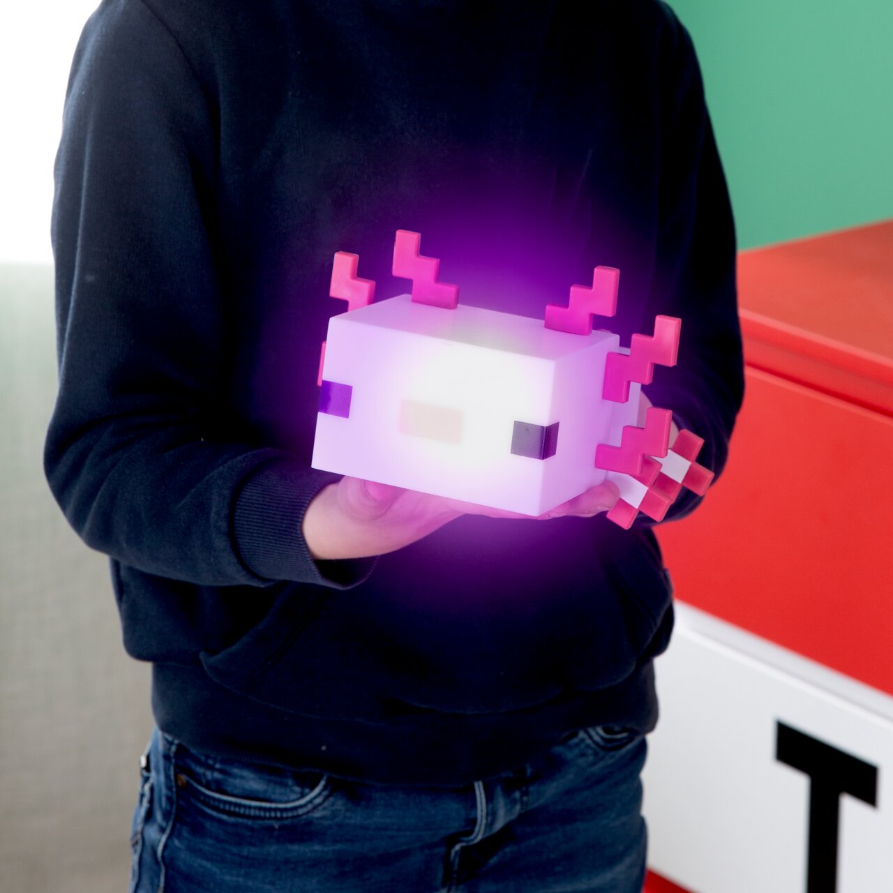 Een persoon houdt een lichtgevende, kubusvormige pixel-lamp in axolotl-stijl met roze kieuwen in zijn handen vooraanzicht vanuit een licht schuin perspectief