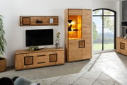 Wohnzimmermöbel aus massivem Holz: Lowboard mit Schubladen und Wandregal neben hoher Vitrine mit warm beleuchteten Glasböden, Frontansicht in leicht schräger Perspektive von links.