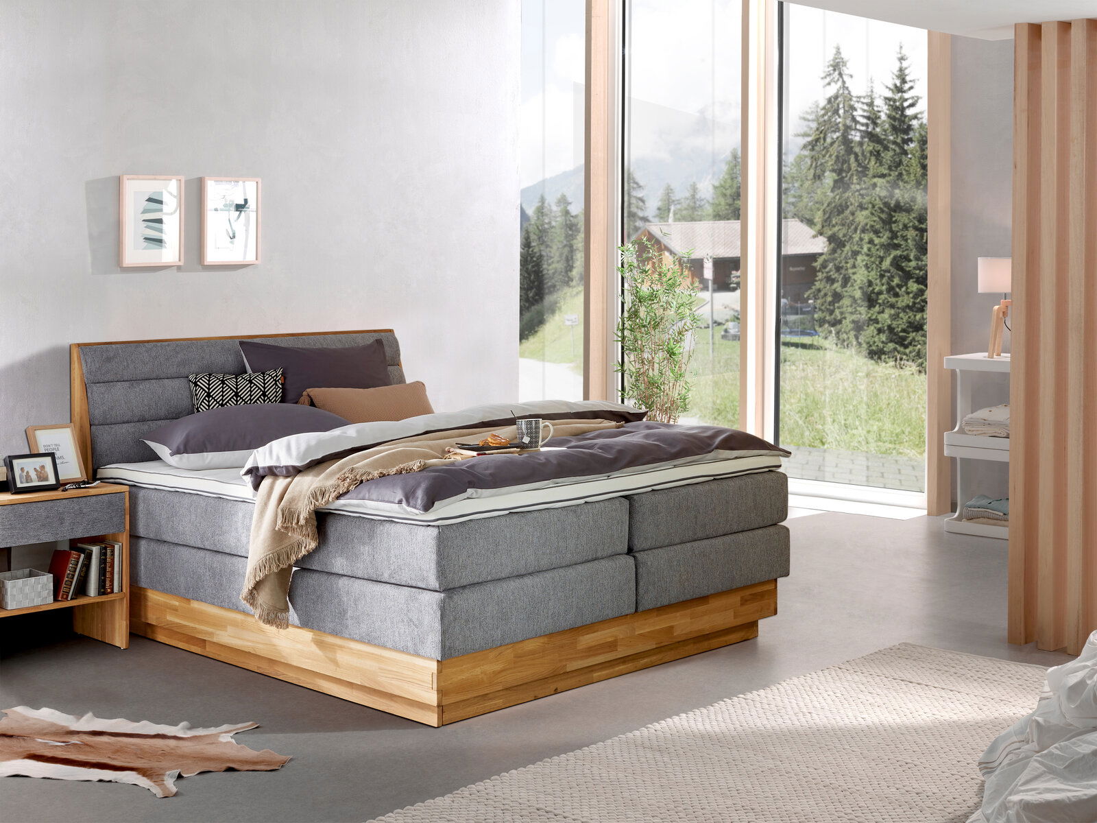 Modernes Boxspringbett in einem hellen Schlafzimmer mit großen Fenstern, seitliche Perspektive