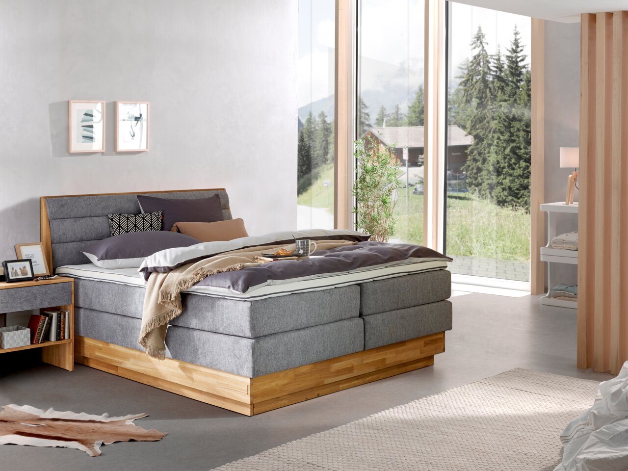 Modernes Boxspringbett in einem hellen Schlafzimmer mit großen Fenstern, seitliche Perspektive