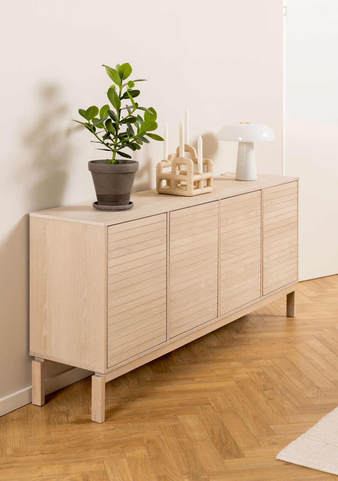 Holz-Sideboard mit vier Türen, dekoriert mit einer Pflanze, Kerzenhalter und Lampe, seitliche Perspektive