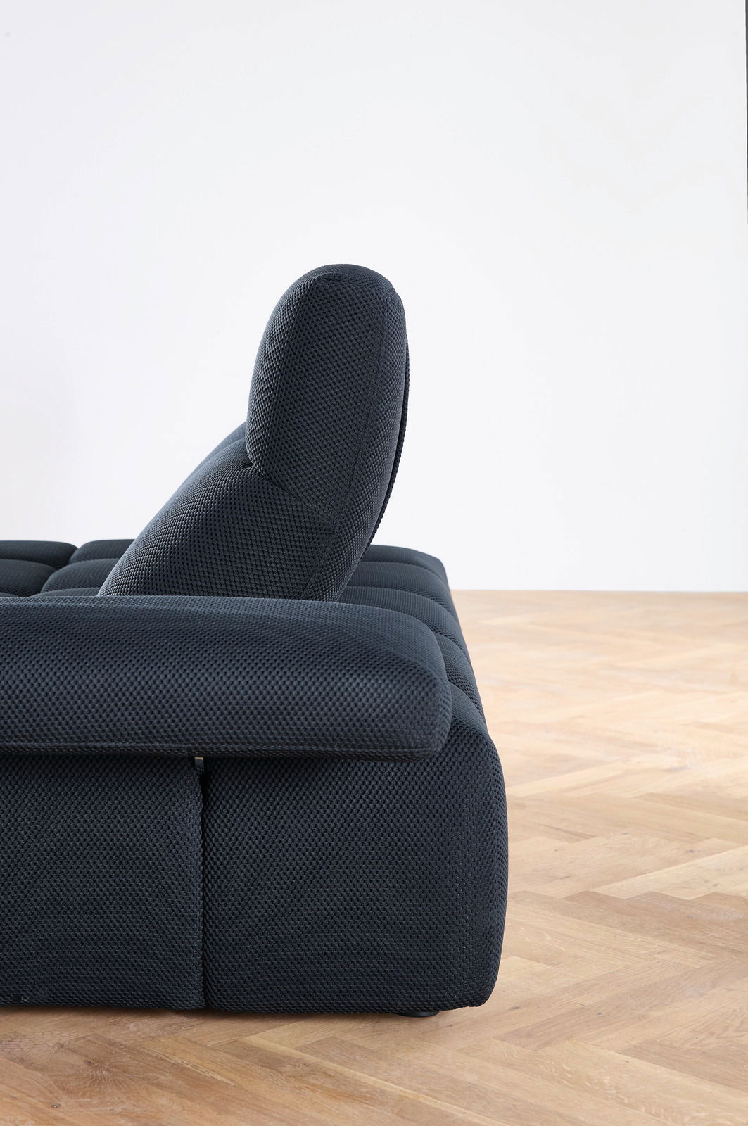 Seitenansicht einer modernen, dunkelgrauen Eckgarnitur mit verstellbarer Rückenlehne auf einem Holzboden.