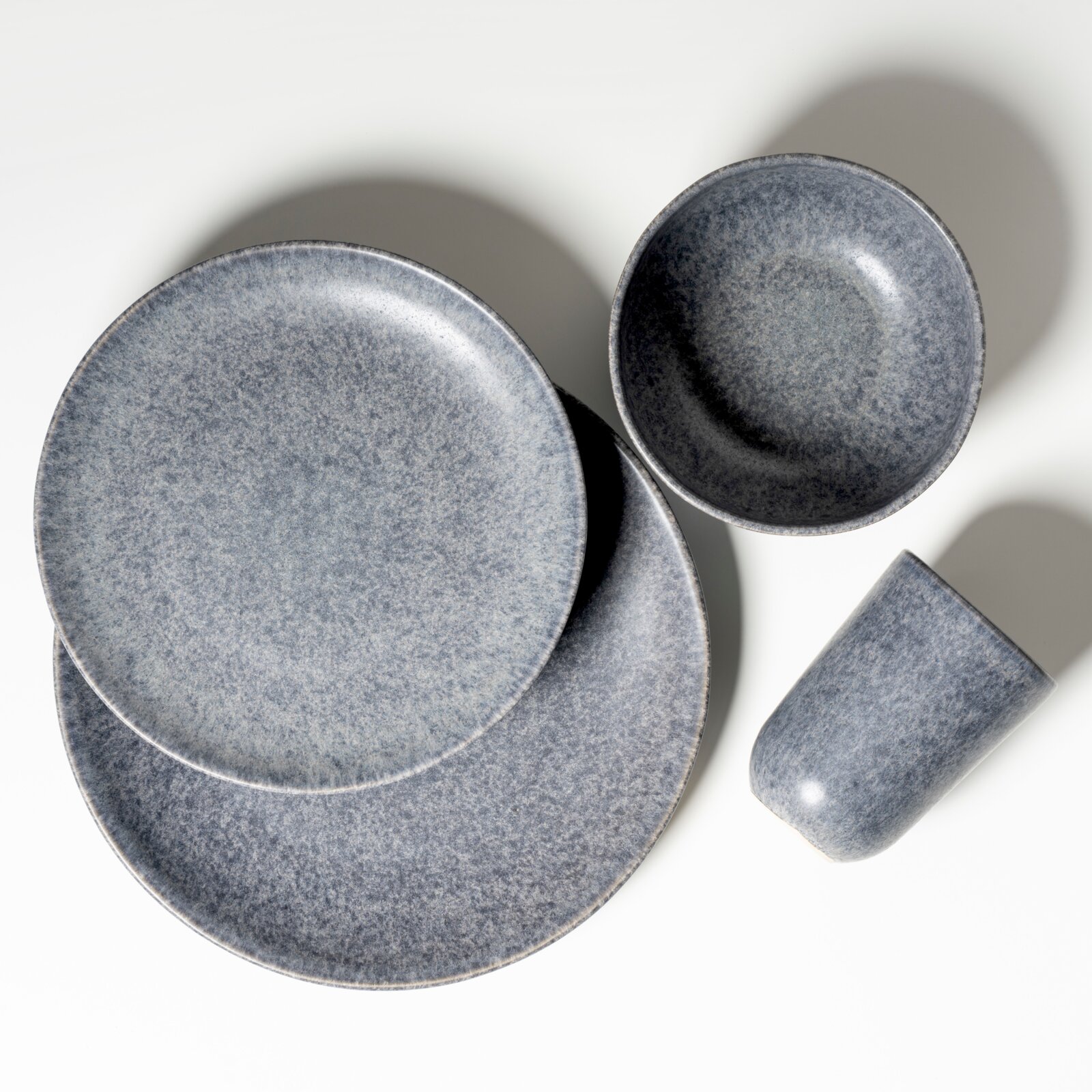 Graues, gesprenkeltes Keramik-Geschirrset mit zwei Tellern, einer Schale und einem Becher auf weißem Hintergrund, fotografiert in Draufsicht (Top-Down).