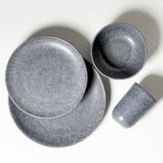 Graues, gesprenkeltes Keramik-Geschirrset mit zwei Tellern, einer Schale und einem Becher auf weißem Hintergrund, fotografiert in Draufsicht (Top-Down).