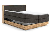 Boxspringbett mit grauem Stoffbezug und Holzrahmen, seitliche Perspektive