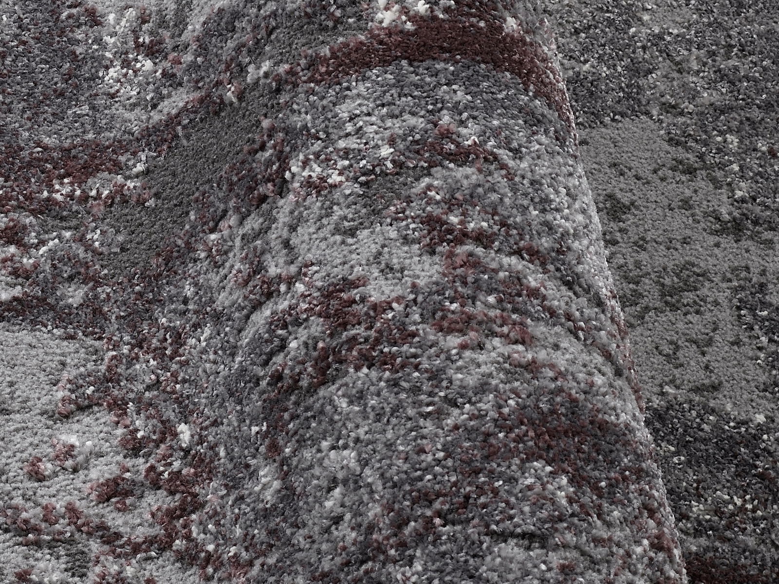 Nahaufnahme eines Designer-Teppichs Juwel Liray in Grautönen mit roten Akzenten, perspektivisch von der Seite aufgenommen.