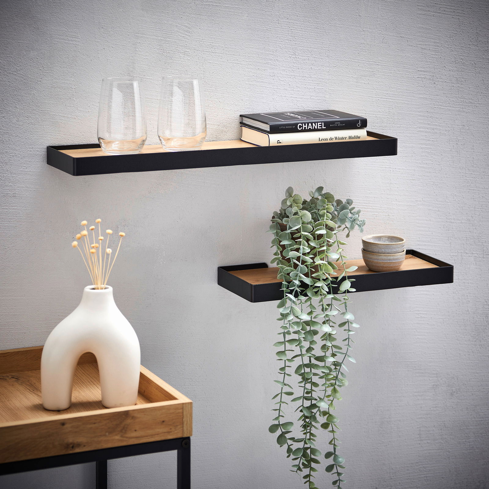 Zwei moderne Wandboards aus Holz und Metall, dekoriert mit Gläsern, Büchern und einer Pflanze, an einer hellen Wand montiert. Perspektive von vorne.