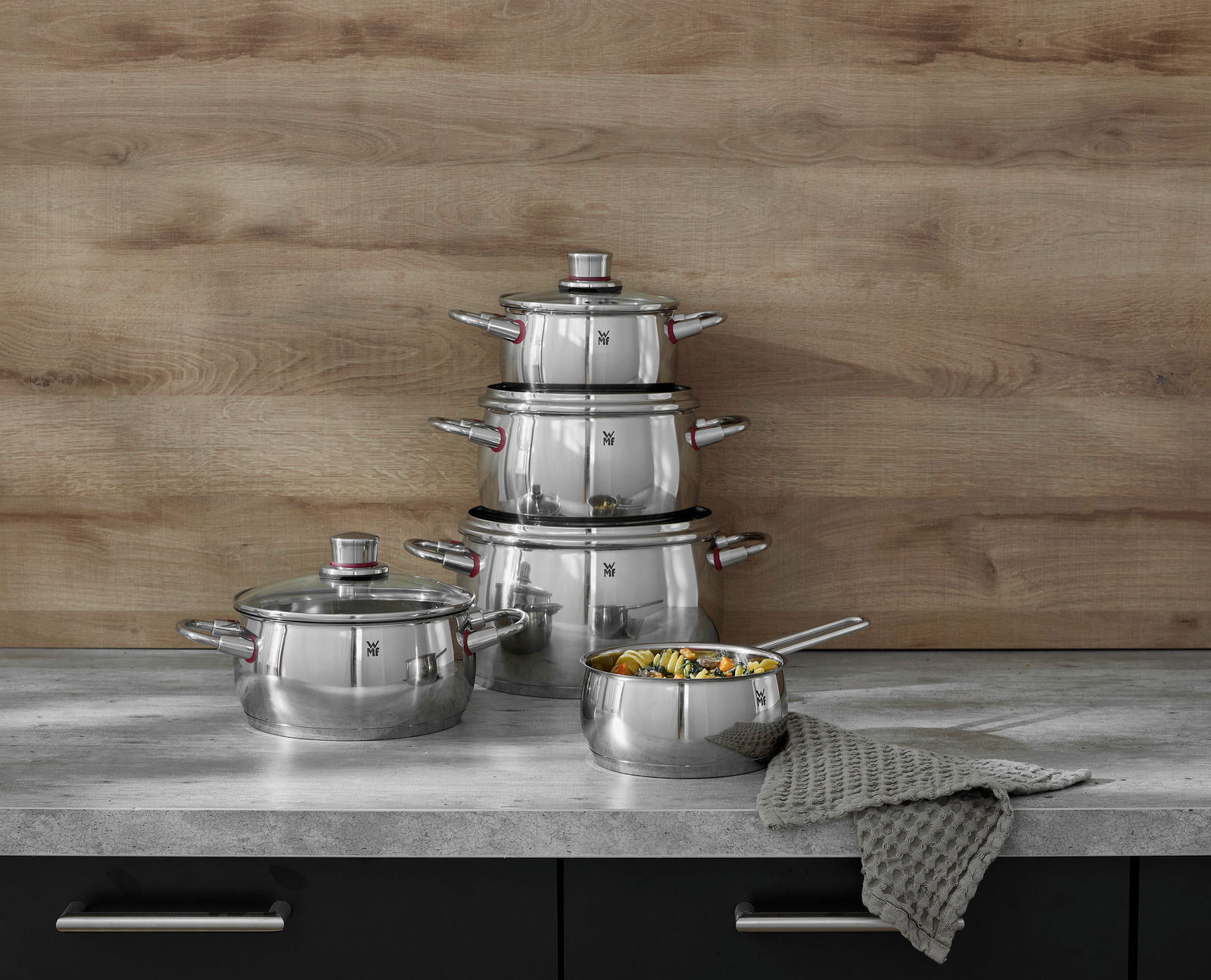 Topfset Quality One 5-tlg. aus Edelstahl, bestehend aus vier Töpfen und einer Stielkasserolle, auf einer Küchenarbeitsplatte vor einer Holzwand, seitliche Perspektive.