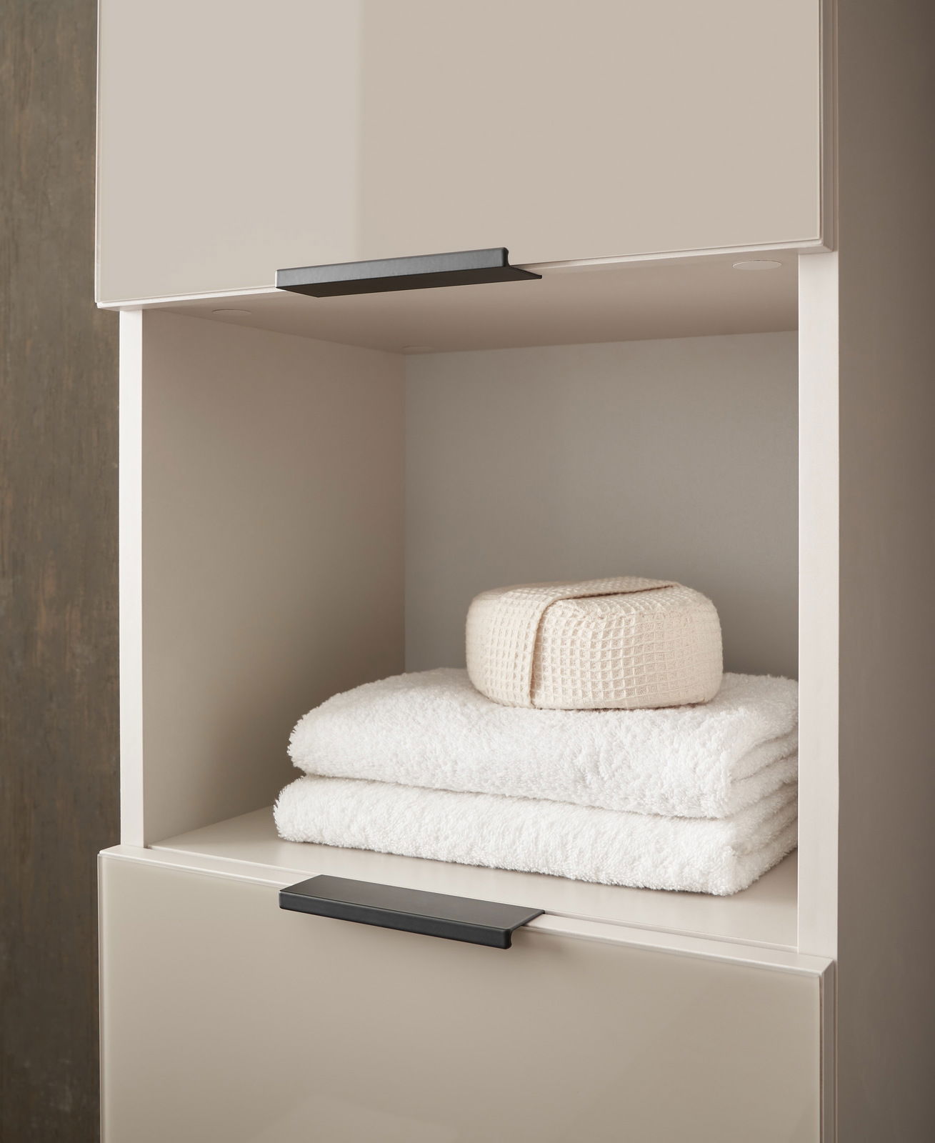 Hochschrank mit offener Ablage, gefüllt mit weißen Handtüchern und einem gefalteten Stoff, seitliche Perspektive
