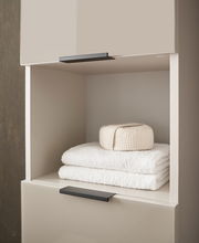 Hochschrank mit offener Ablage, gefüllt mit weißen Handtüchern und einem gefalteten Stoff, seitliche Perspektive