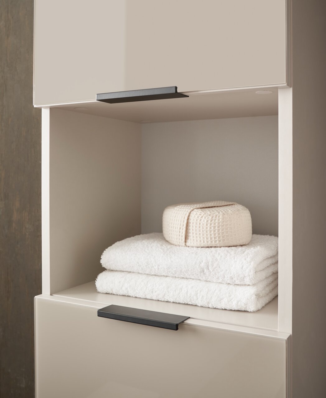Hochschrank mit offener Ablage, gefüllt mit weißen Handtüchern und einem gefalteten Stoff, seitliche Perspektive