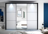 Moderner Kleiderschrank mit Schiebetüren und integriertem Spiegel, frontal fotografiert. Der Schrank ist in einem stilvollen Raum mit blauer Wand und dekorativen Elementen platziert.