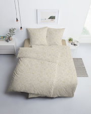 Beige Bettwäsche mit filigranem floralem Muster und passenden Kissenbezügen, schräg von vorn in einem hellen Schlafzimmer dargestellt