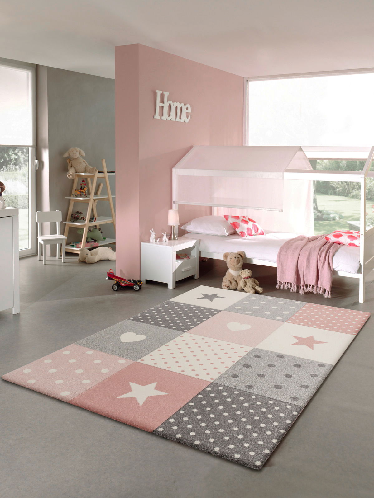 Kinderzimmer mit einem pastellfarbenen Teppich im Vordergrund, der Sterne und Punkte in Rosa, Grau und Weiß zeigt. Der Teppich liegt auf einem grauen Boden, umgeben von einem Bett, Spielzeug und Dekorationen in einem hellen, freundlichen Raum.