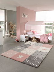 Kinderzimmer mit einem pastellfarbenen Teppich im Vordergrund, der Sterne und Punkte in Rosa, Grau und Weiß zeigt. Der Teppich liegt auf einem grauen Boden, umgeben von einem Bett, Spielzeug und Dekorationen in einem hellen, freundlichen Raum.