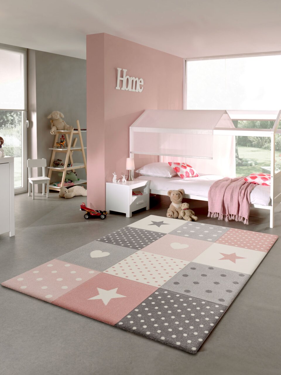 Kinderzimmer mit einem pastellfarbenen Teppich im Vordergrund, der Sterne und Punkte in Rosa, Grau und Weiß zeigt. Der Teppich liegt auf einem grauen Boden, umgeben von einem Bett, Spielzeug und Dekorationen in einem hellen, freundlichen Raum.