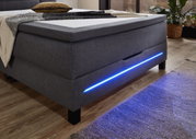 Boxspringbett in grauem Stoff mit blauer LED-Beleuchtung, seitliche Perspektive