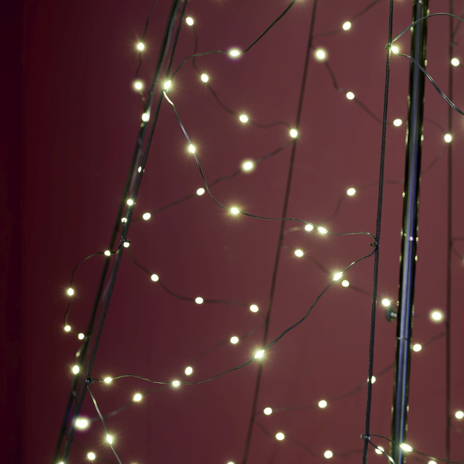 Detailopname vanuit vooraanzicht van een lichtsnoer met warmwitte leds en donkere kabels tegen een bordeauxrode achtergrond