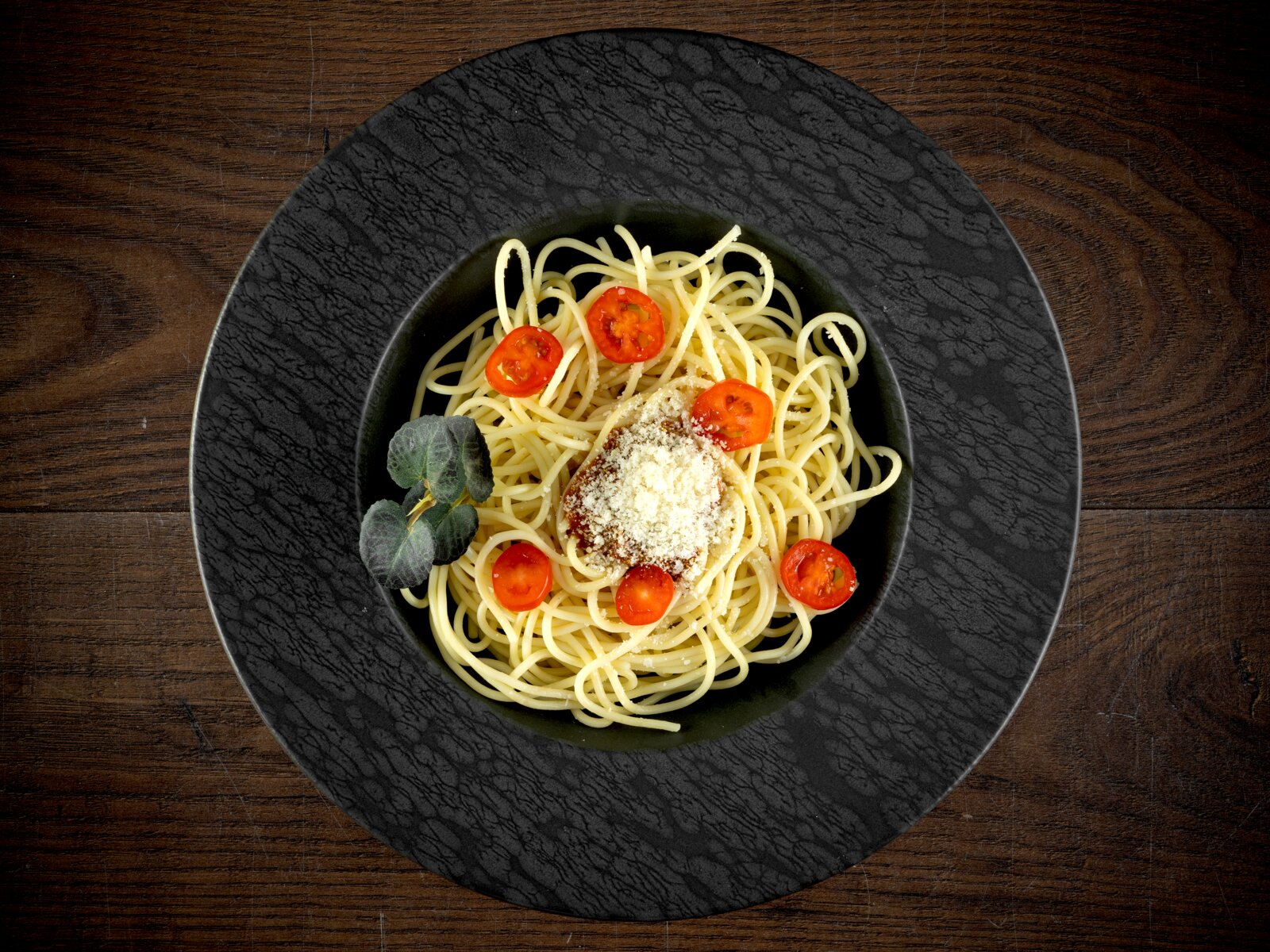Creatable Pastateller 2-tlg SCHIEFER Spaghetti auf schwarzem Teller mit Tomatenscheiben, geriebenem Käse und Kräuterblatt auf Holztisch, Draufsicht von oben