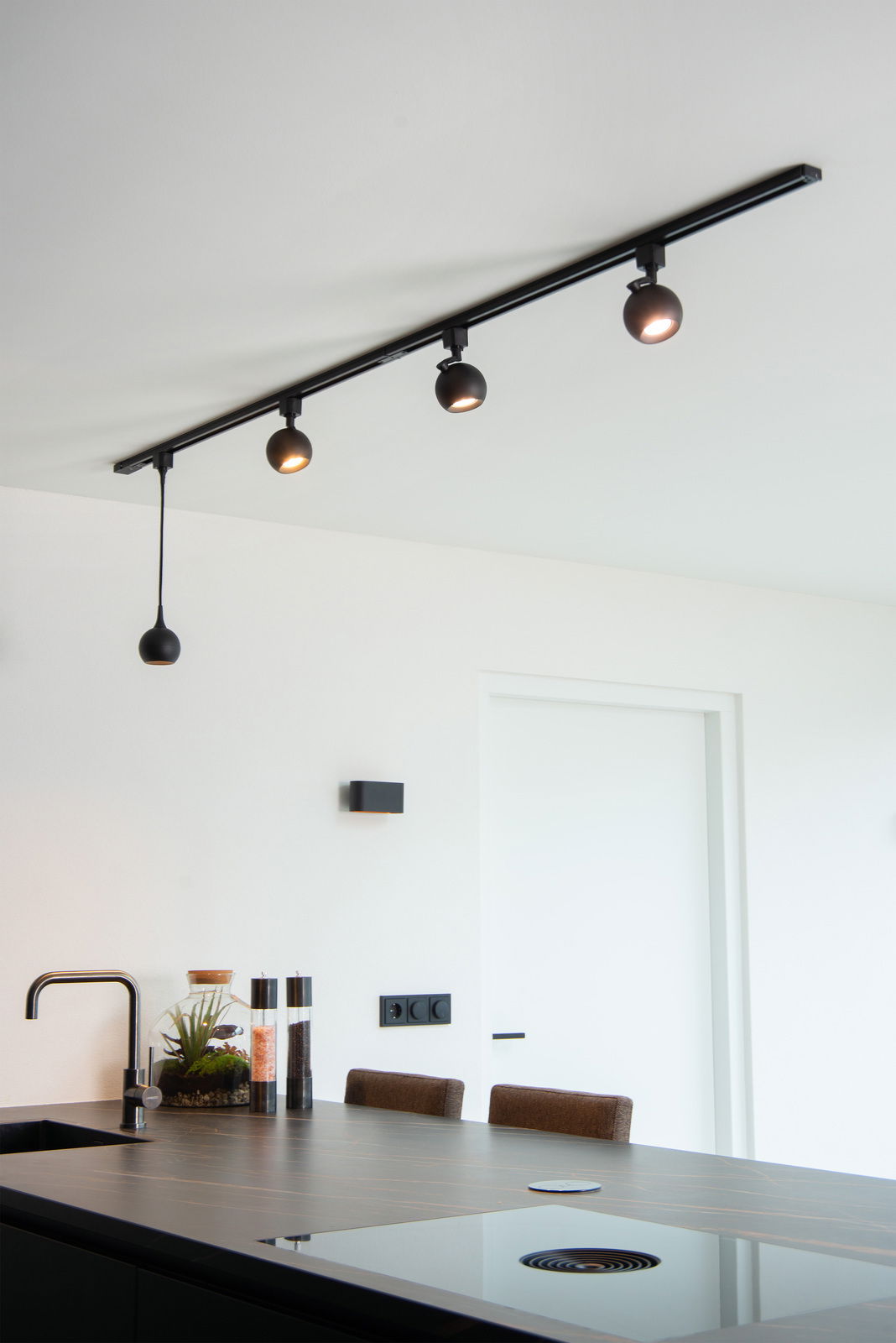 Moderne schwarze Pendelleuchte FAVORI in einer Küche, von unten fotografiert, mit drei Strahlern an einer Schiene und einem hängenden Lampenschirm.