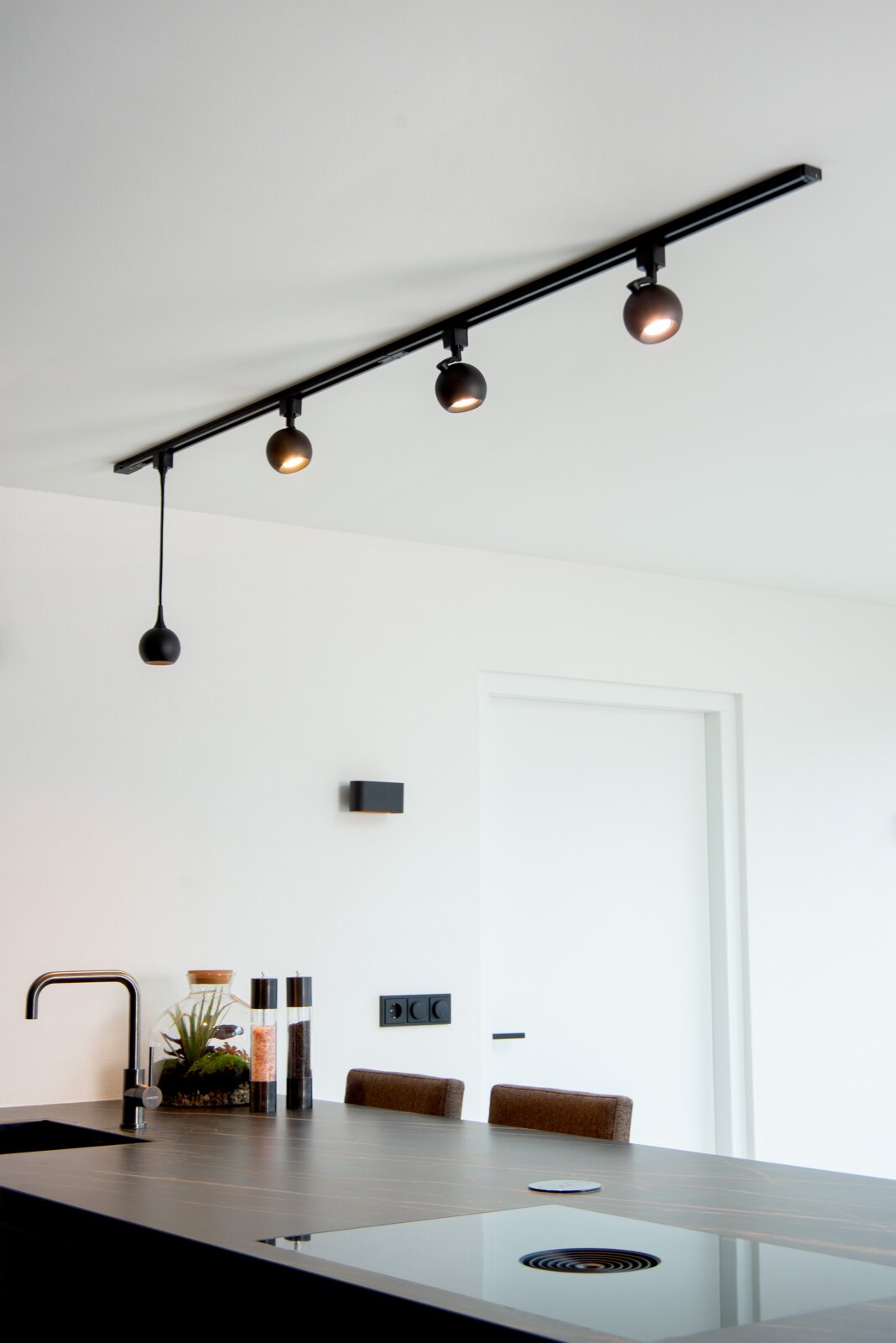Moderne schwarze Pendelleuchte FAVORI in einer Küche, von unten fotografiert, mit drei Strahlern an einer Schiene und einem hängenden Lampenschirm.