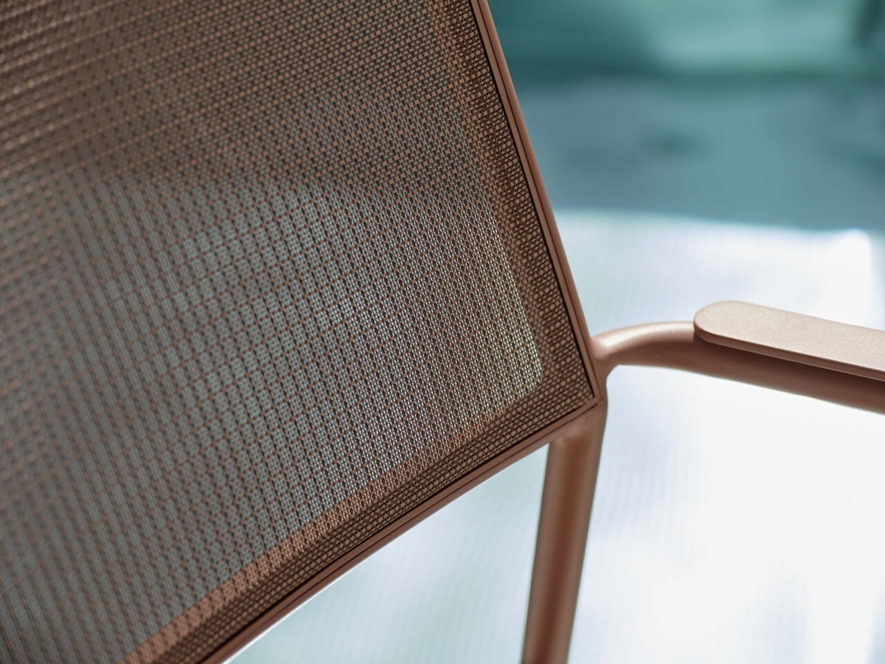 Nahaufnahme eines Stapelsessels mit braunem Netzgewebe und Armlehne, seitliche Perspektive