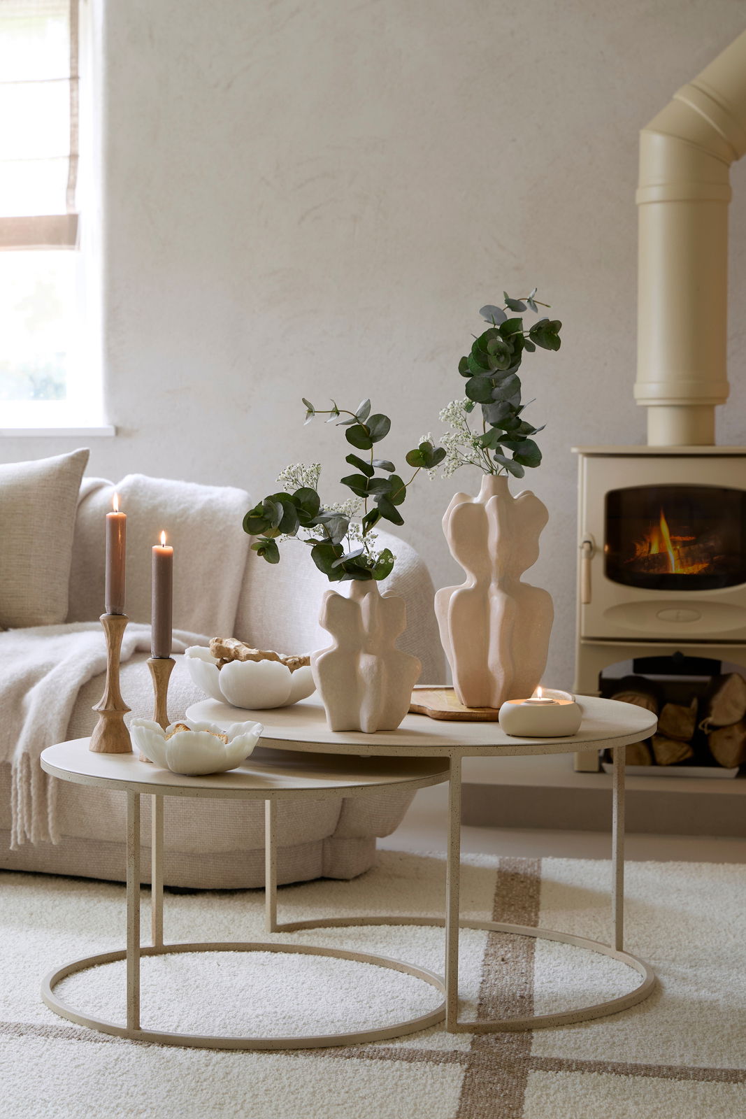 Zwei elegante Kerzenständer aus Holz auf einem Couchtisch, umgeben von dekorativen Vasen und einem gemütlichen Kamin im Hintergrund. Perspektive: seitlich.