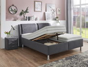 Graues Polsterbett mit verstellbarem Lattenrost, seitlicher Perspektive, in modernem Schlafzimmer mit Nachttisch und Dekoration.