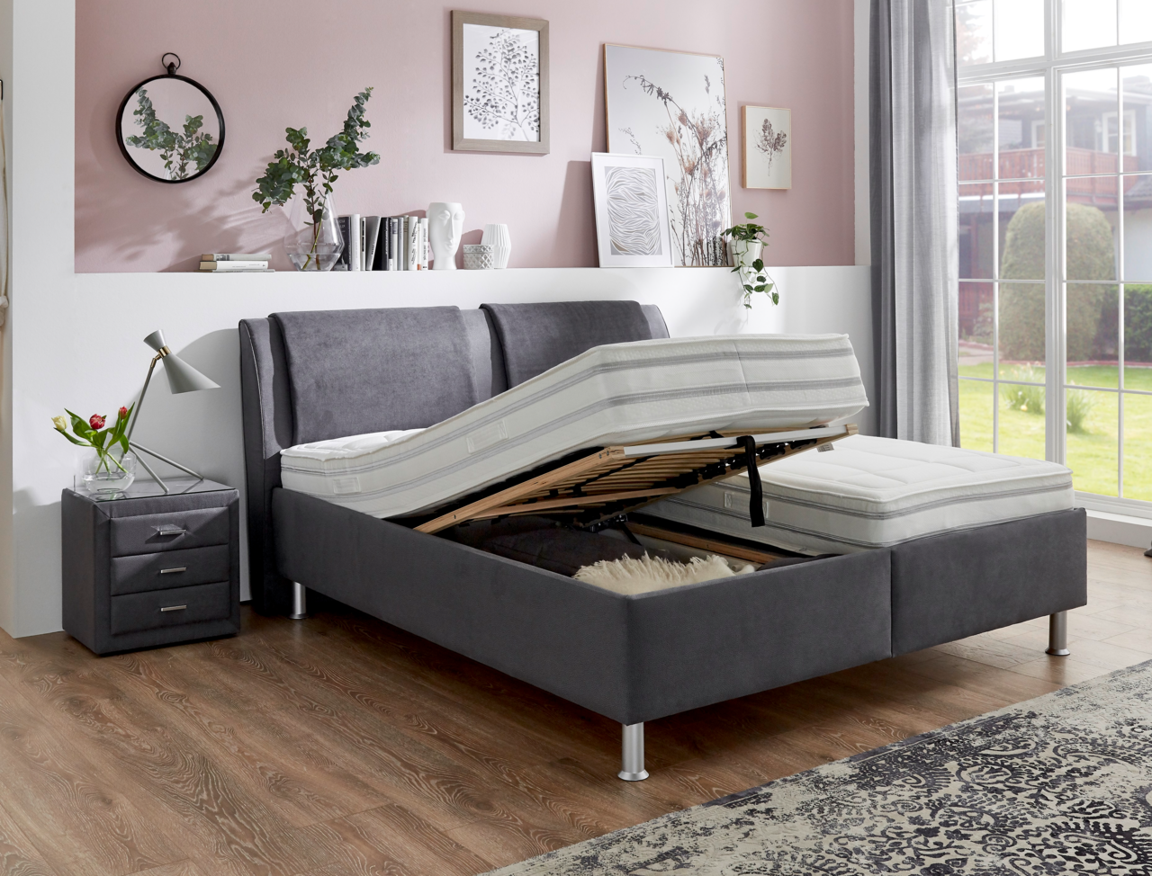 Graues Polsterbett mit verstellbarem Lattenrost, seitlicher Perspektive, in modernem Schlafzimmer mit Nachttisch und Dekoration.