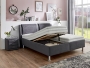 Graues Polsterbett mit verstellbarem Lattenrost, seitlicher Perspektive, in modernem Schlafzimmer mit Nachttisch und Dekoration.