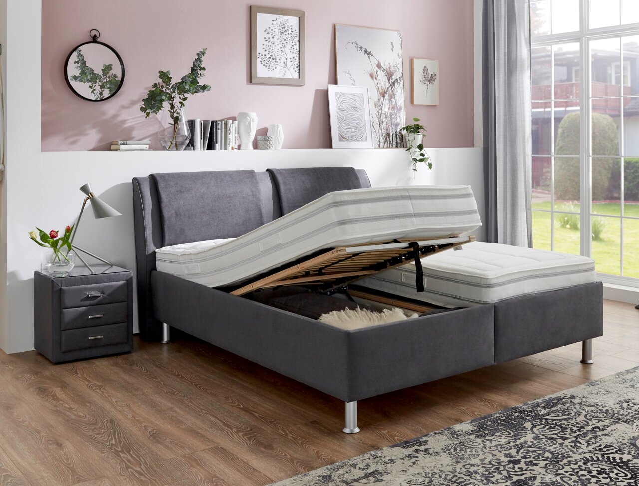 Graues Polsterbett mit verstellbarem Lattenrost, seitlicher Perspektive, in modernem Schlafzimmer mit Nachttisch und Dekoration.