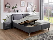 Graues Polsterbett mit verstellbarem Lattenrost, seitlicher Perspektive, in modernem Schlafzimmer mit Nachttisch und Dekoration.