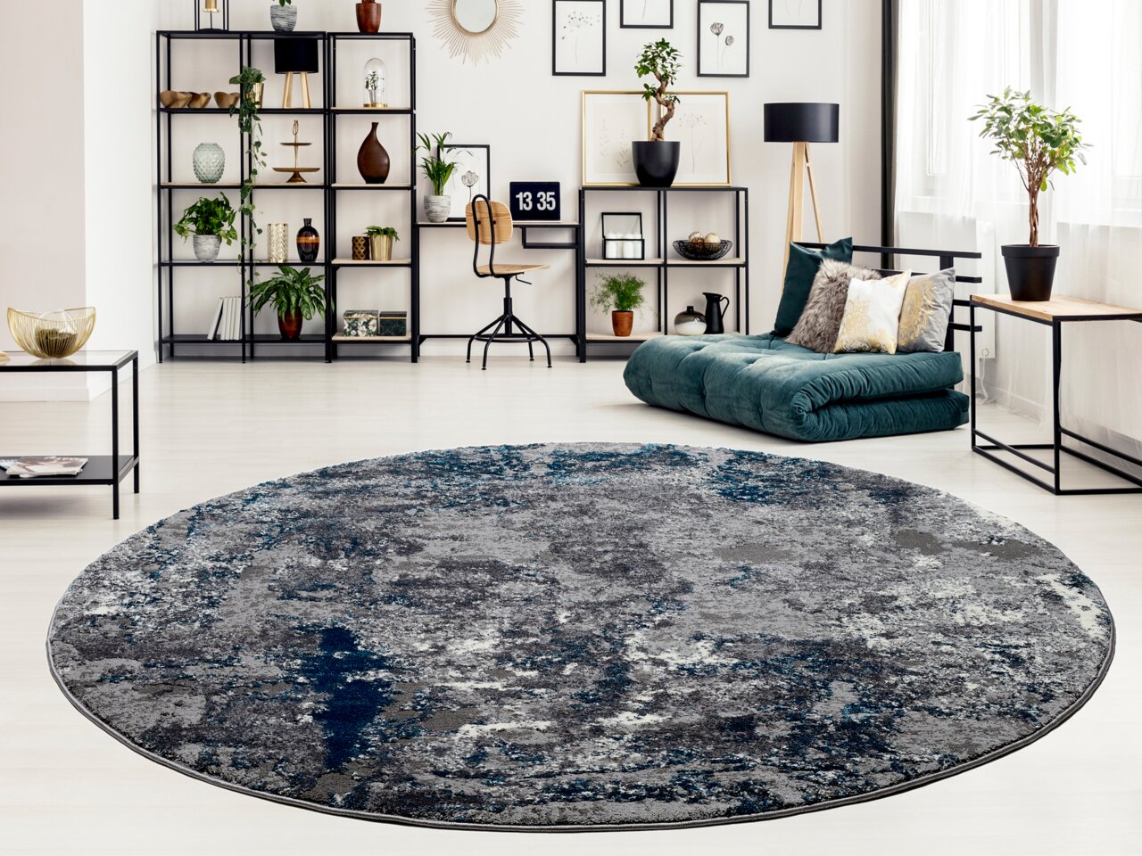 Runder Designer Teppich in Grau- und Blautönen in einem modernen Wohnzimmer mit Blick auf ein Regal, eine grüne Couch und Pflanzen.